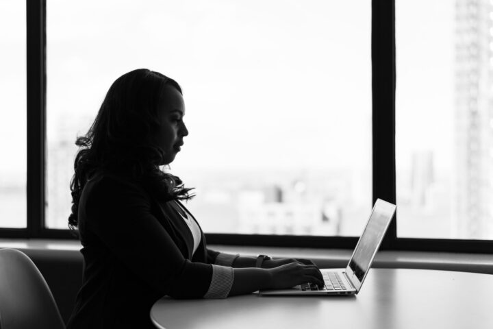 Zwart-wit afbeelding van een vrouw die in een moderne kantooromgeving op haar laptop werkt.