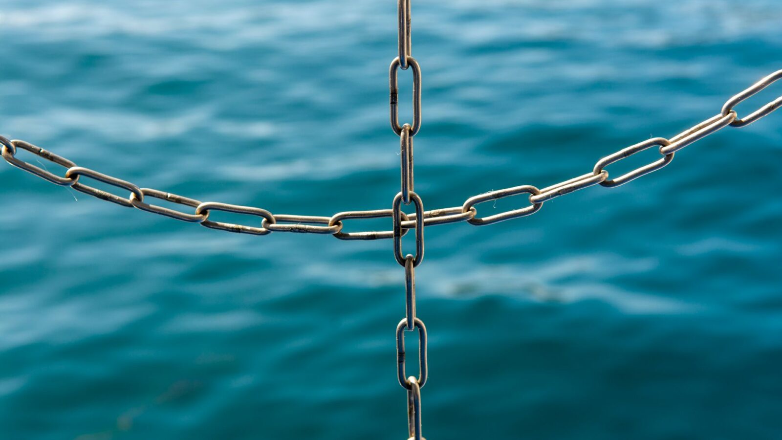 Close-up van onderling verbonden metalen kettingen met de zee vervaagd op de achtergrond.