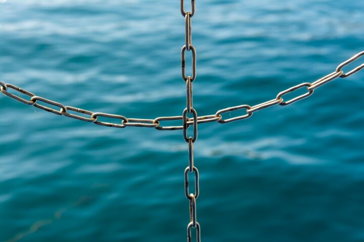 Close-up van onderling verbonden metalen kettingen met de zee vervaagd op de achtergrond.