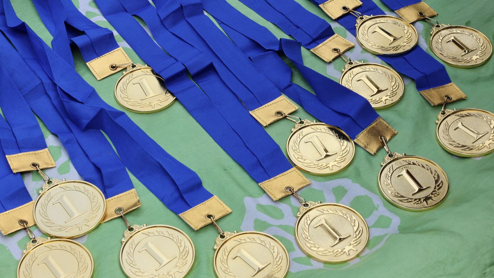 Meerdere gouden medailles met blauwe linten op een groen oppervlak, symboliseren de overwinning.