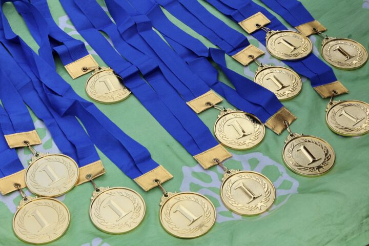 Meerdere gouden medailles met blauwe linten op een groen oppervlak, symboliseren de overwinning.