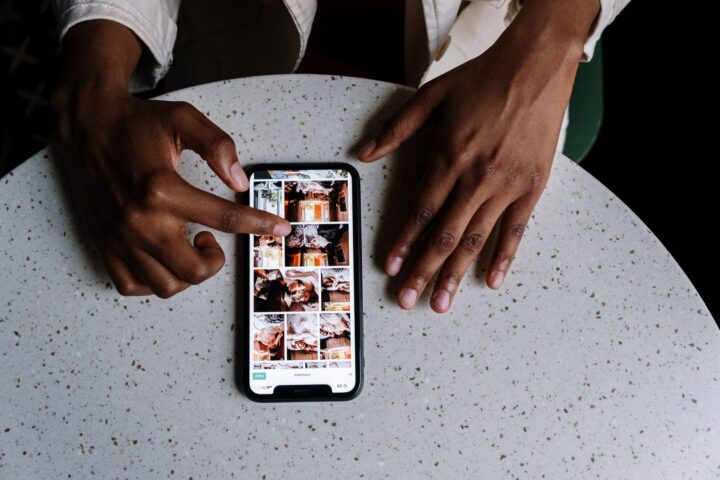 Handen die interageren met smartphone die sociale media-inhoud toont op tafel in een cafeë-omgeving.