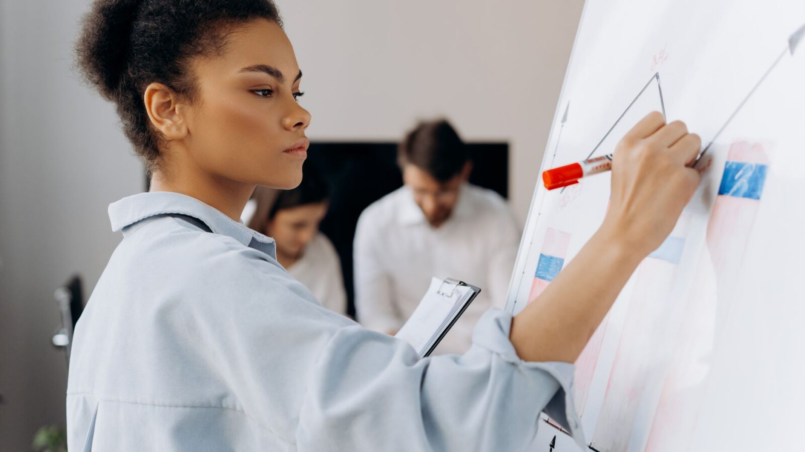 Zelfverzekerde zakenvrouw illustreert gegevens op het whiteboard tijdens een teamvergadering en toont gezamenlijke analyse.