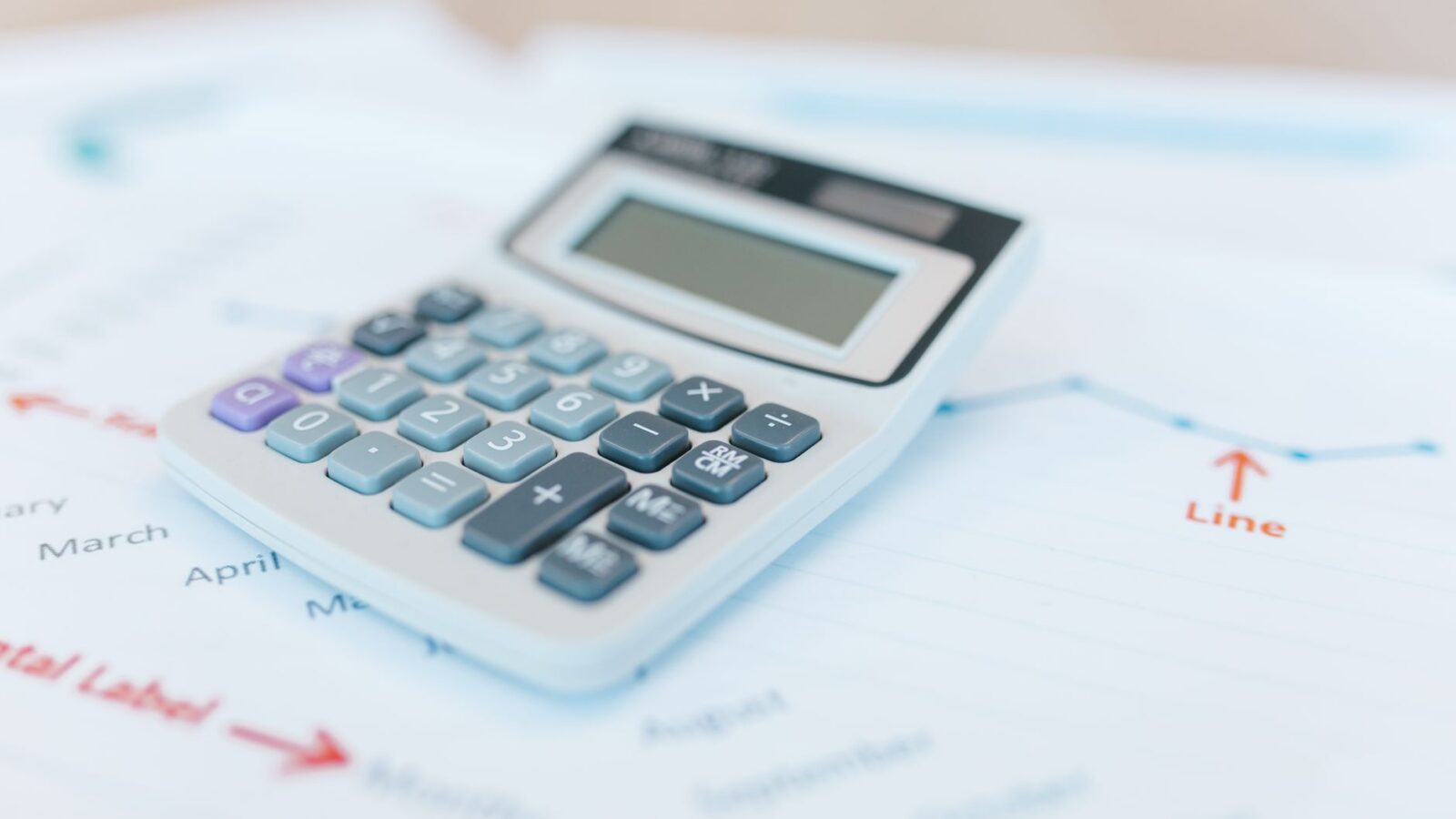 Close-up van een rekenmachine op financiële documenten met grafieken en analysepapieren.