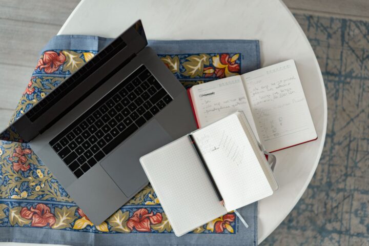 Bovenaanzicht van een laptop met notitieboeken en een potlood op een gedessineerde stof.