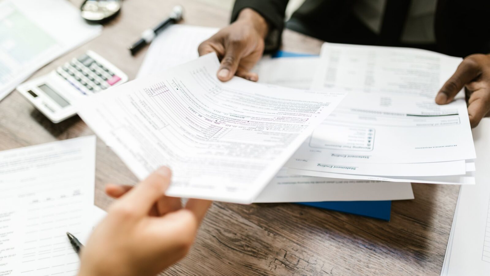 Twee professionals wisselen documenten uit in een kantooromgeving, met de nadruk op papierwerk en data-analyse.
