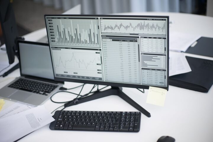 Een professionele werkruimte met computers en analytische grafieken op een monitor, die de moderne zakelijke omgeving symboliseert.